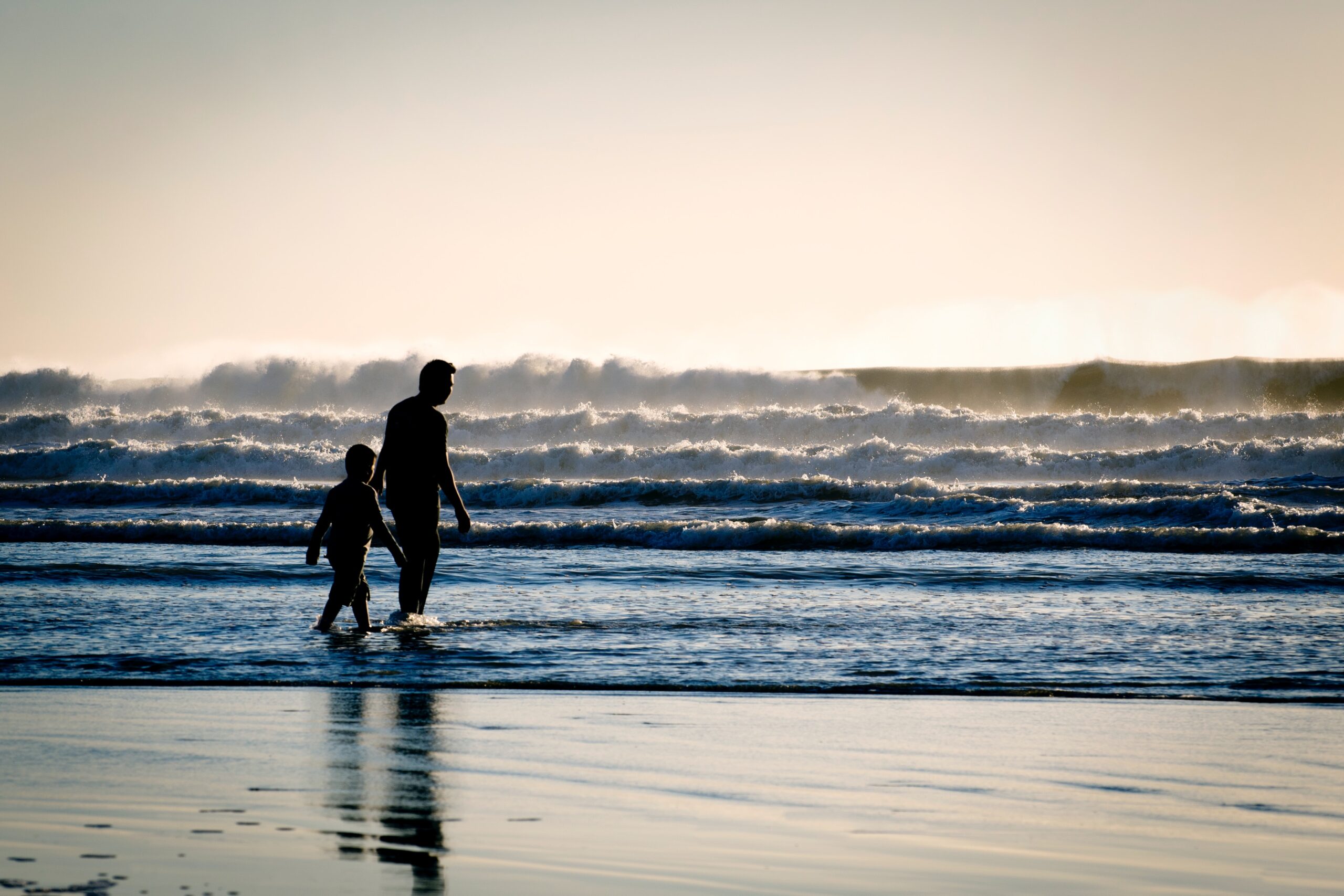 father and son silhouetted and walking on a beach