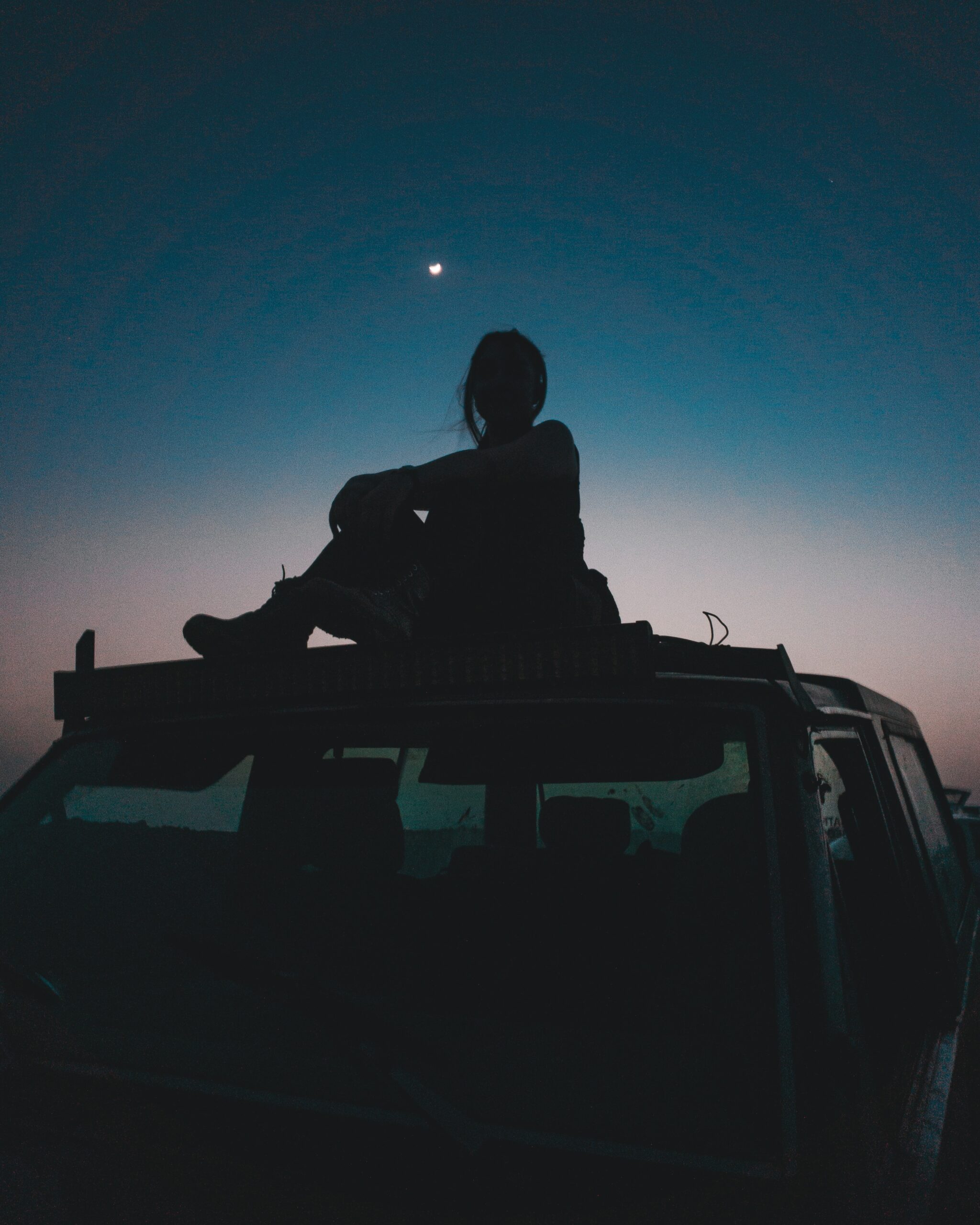 a woman sitting on the roof of a car under the night sky