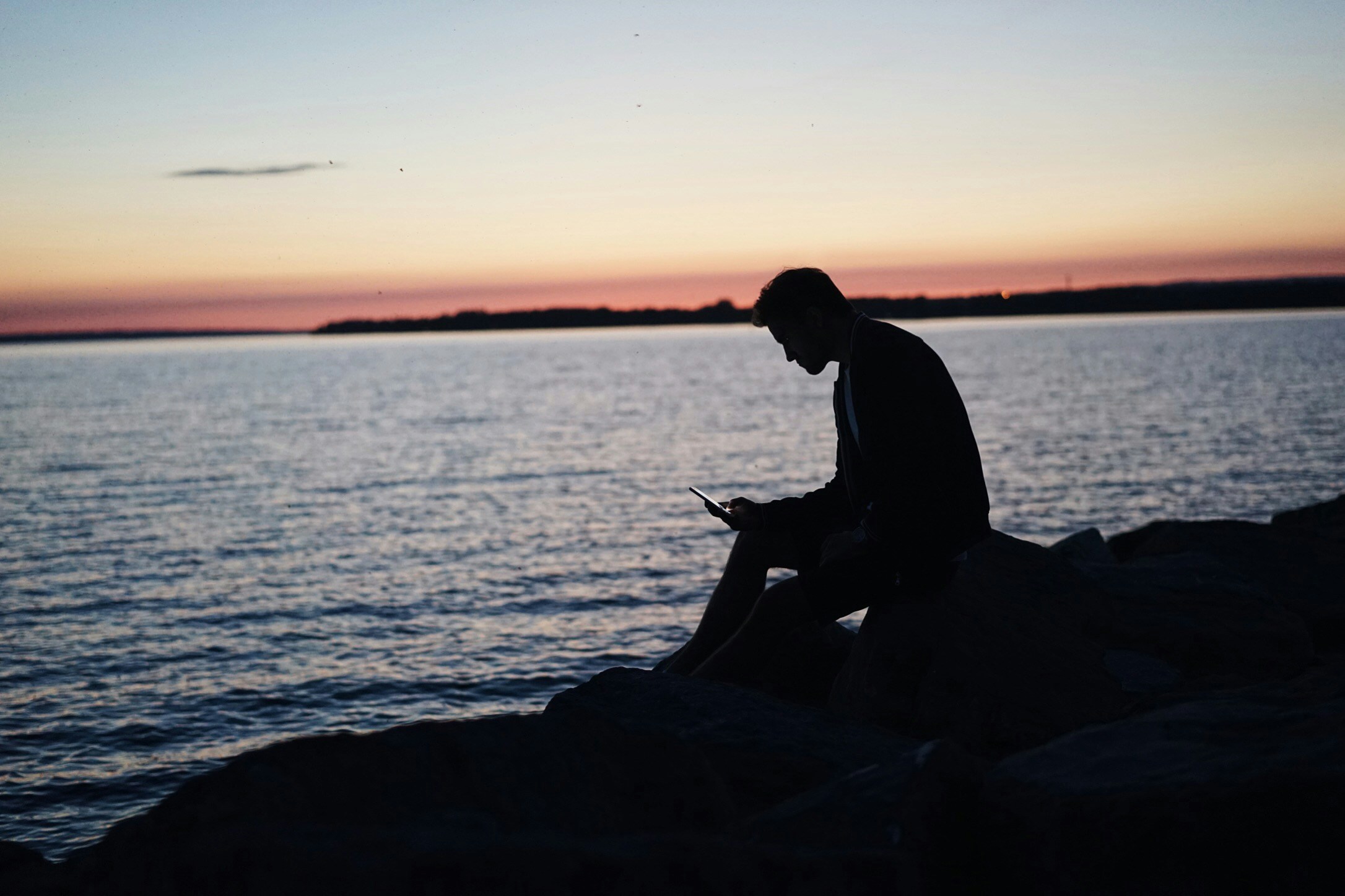 Man sitting on a beach looking at a phone.